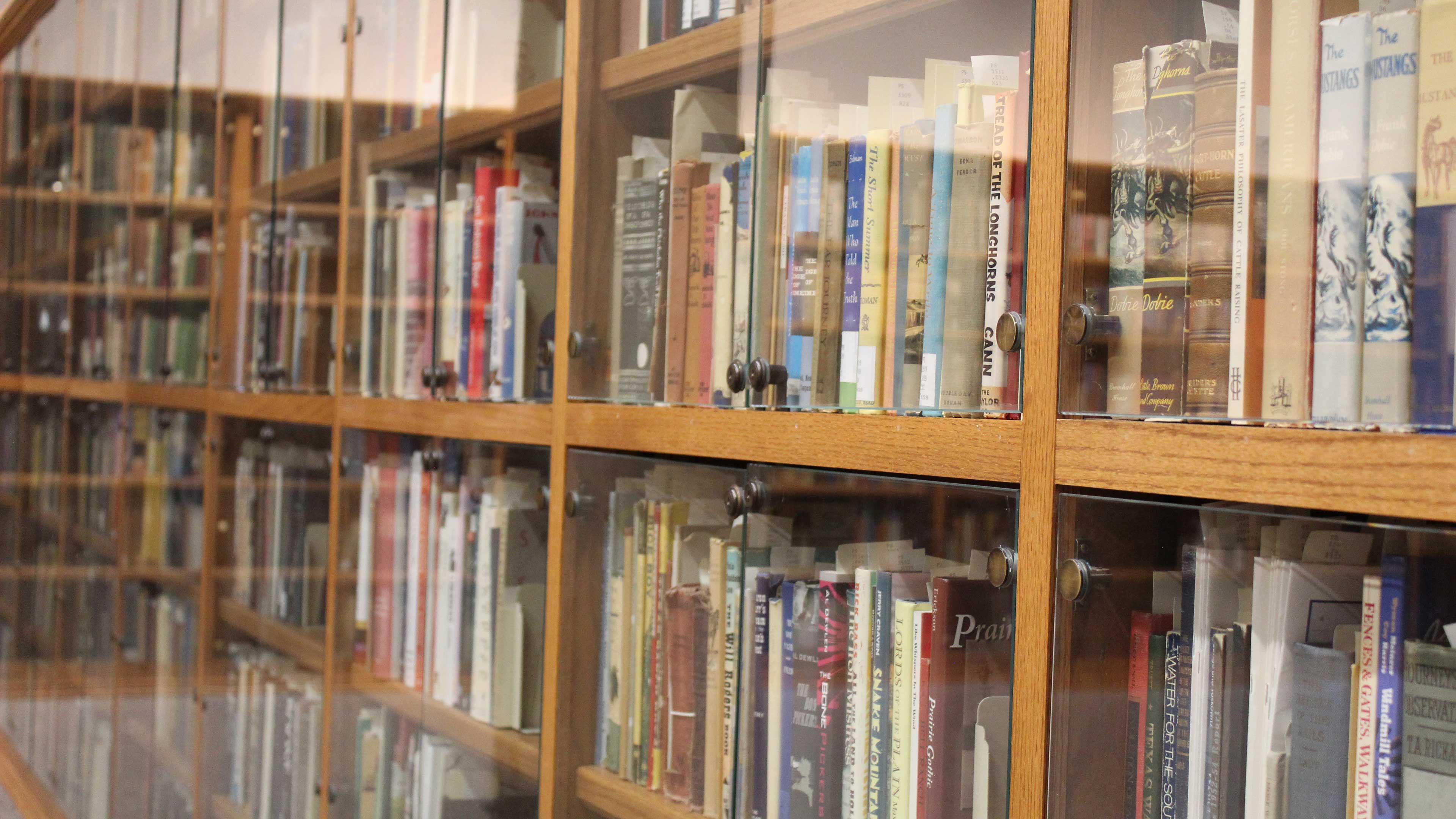 Books on a long wooden bookcase with glass protection located in the Blackburn Room